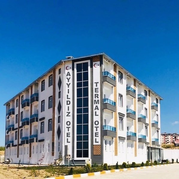 Un hotel de varios pisos con balcones, un letrero vertical en el centro y un cielo despejado.