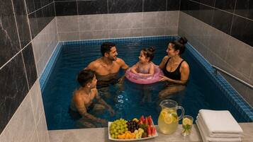 Eine Familie in einer kleinen, gefliesten Whirlpool-Badewanne mit einer Obstplatte und Getränken.
