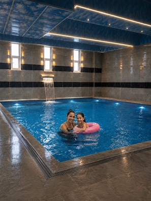 Piscina interior con fuente, paredes de azulejos y ventanas.