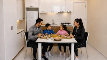 En familie spiser ved et bord i et moderne køkken med hvide skabe, en gasovn og et køleskab.