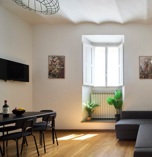 A room with a dining table, chairs, a sofa, a window with open shutters, and two wall-mounted paintings. - A comfortable stay, easy self-check-in, and a great location for exploring Florence. (Firenze)