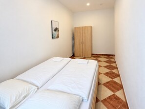 A small, clean room with two beds, a wardrobe, and a painting on the wall. - Make Vienna Home 1BR with Living Room (Vienna)