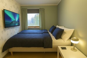 A bedroom with a bed, a TV on the wall, a window with curtains, a bedside lamp, and a nightstand. - Northern Lights Apt Midtgaard · 2BR · Free Parking · Kvaløya Tromsø (Tromsø)