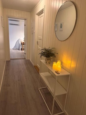 A hallway with wooden flooring, a white console table with candles, a mirror, and a door leading to another room. - Northern Lights Apt Midtgaard · 2BR · Free Parking · Kvaløya Tromsø (Tromsø)