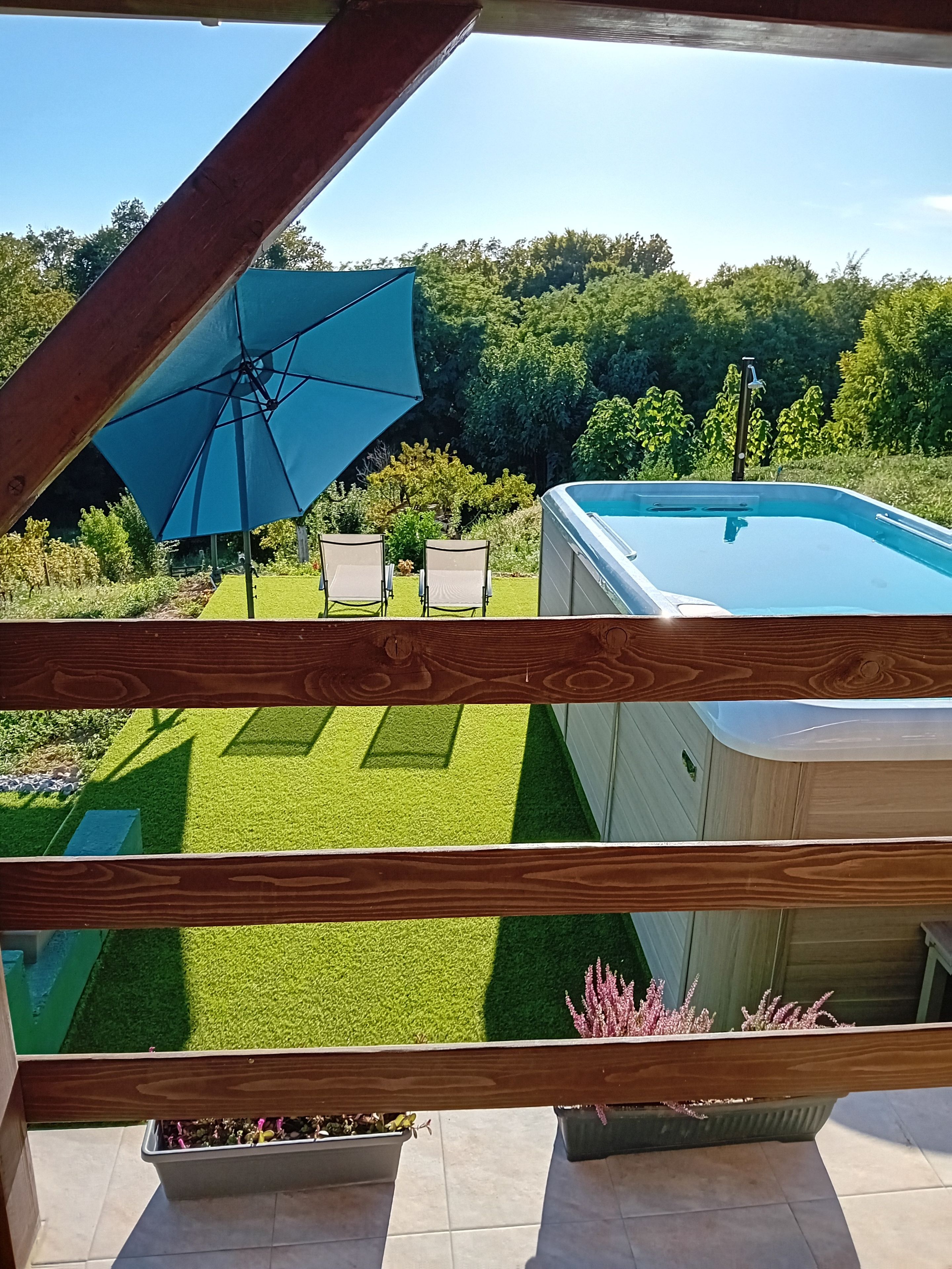Uitzicht vanaf een balkon op een zwembad, een gazon en een houten terras.
