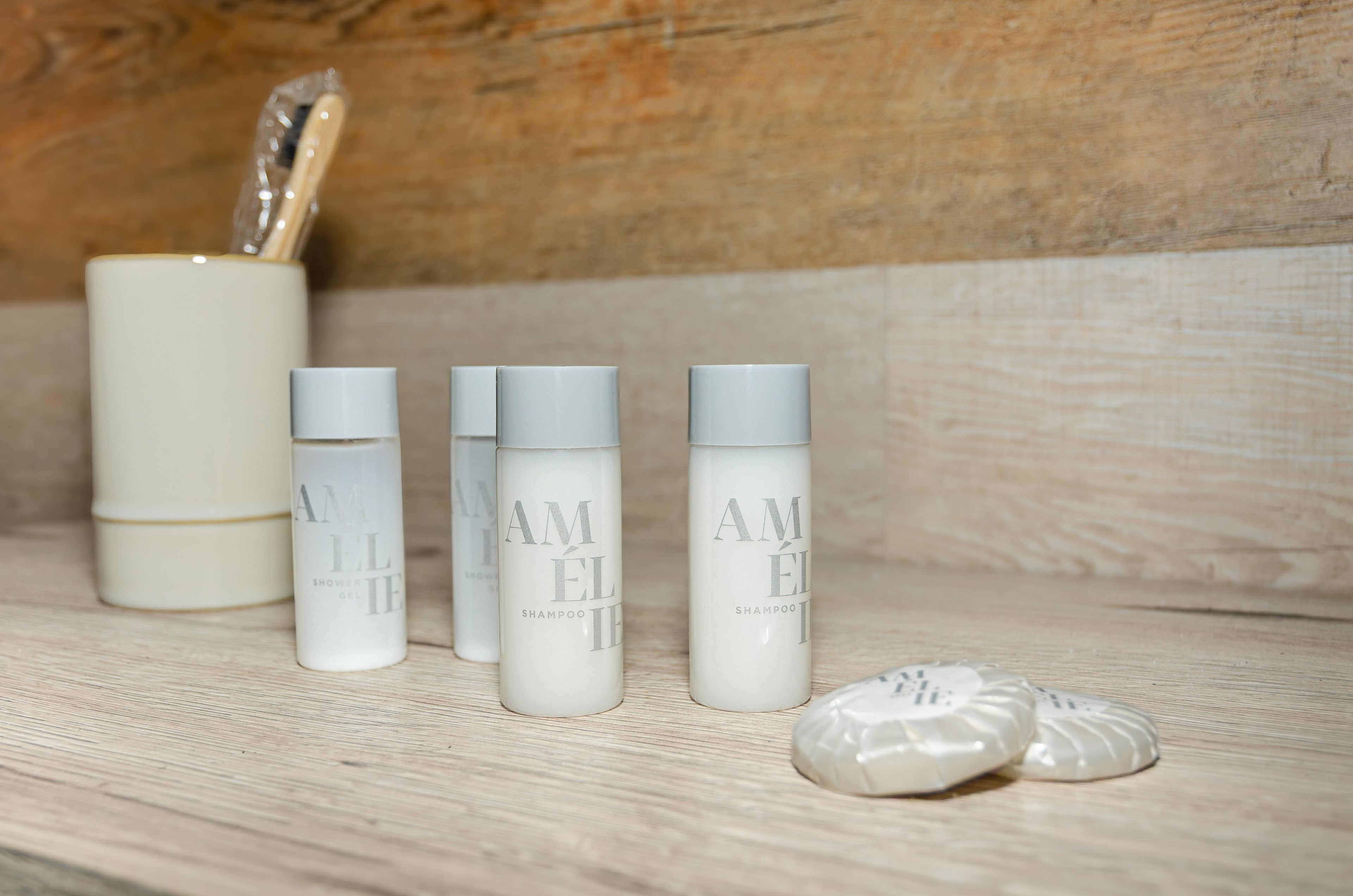 Een houten plank met vier witte flessen met de tekst 'AMELIE SHAMPOO' en een witte verpakking met een zilveren deksel.
