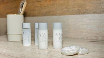 Een houten plank met vier witte flessen met de tekst 'AMELIE SHAMPOO' en een witte verpakking met een zilveren deksel.