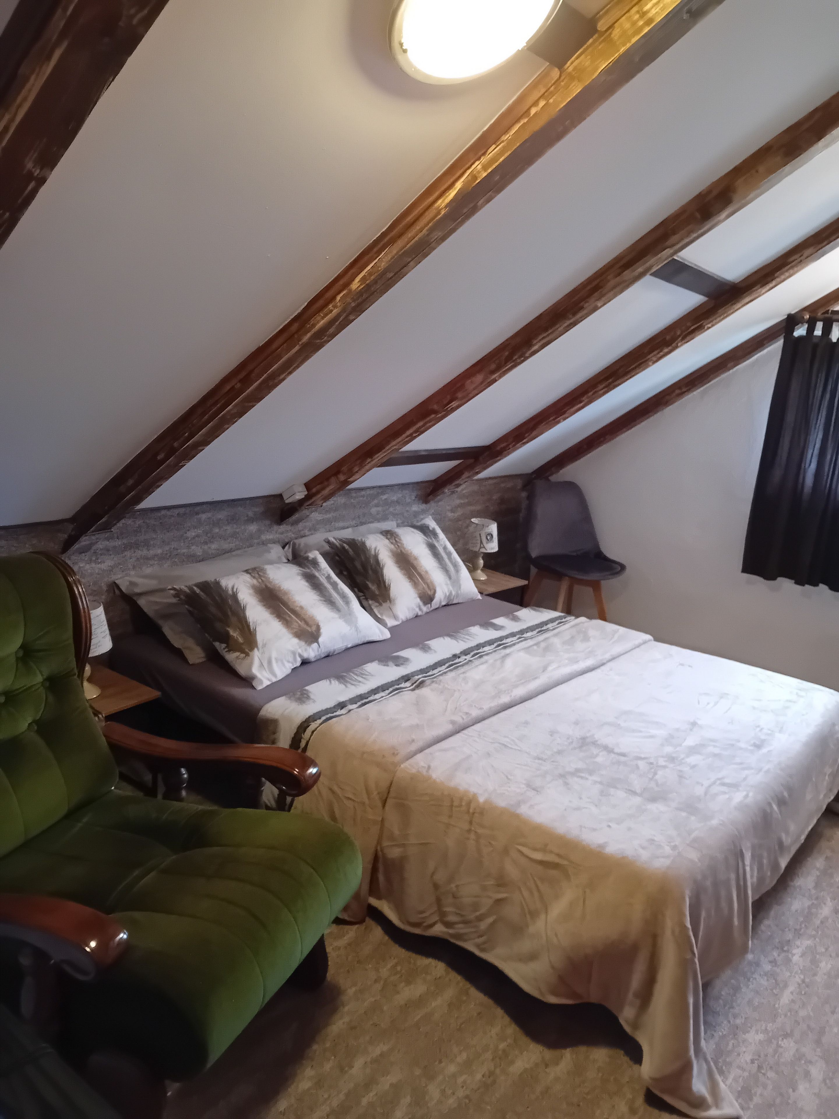 Een slaapkamer met een bed, een groene fauteuil, een nachtkastje en een raam met gordijnen.
