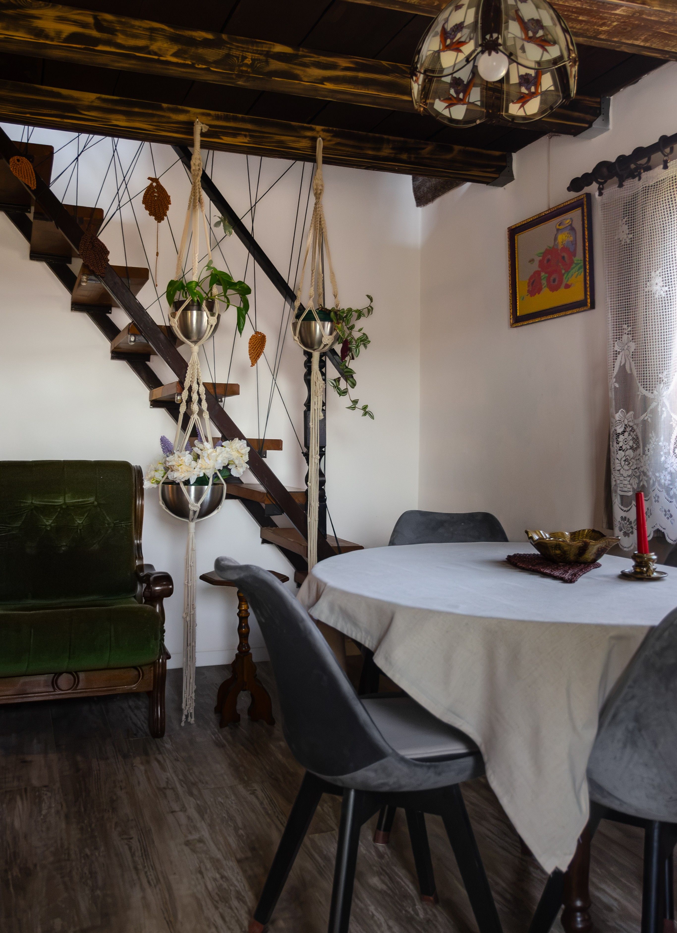 Un coin repas avec une table ronde, des chaises, un canapé vert et un escalier décoré de motifs en macramé.