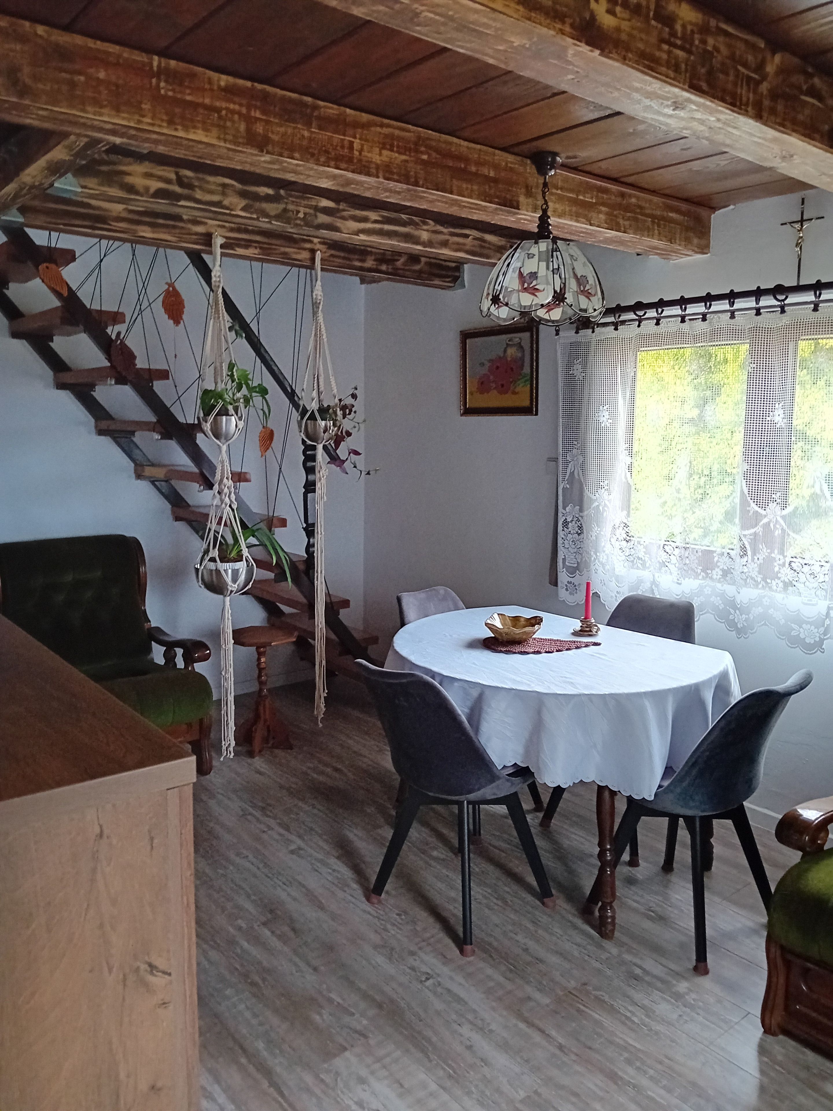 Een eetruimte met een ronde tafel, stoelen, een kroonluchter en een trap versierd met macramé.