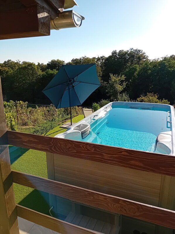 A hot tub with a clear blue pool, surrounded by a wooden deck and a blue umbrella.