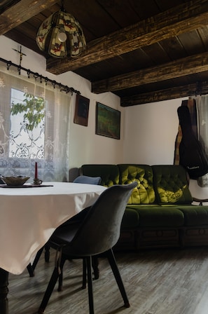 A dining area with a table, chairs, a green sofa, and a hanging lamp.