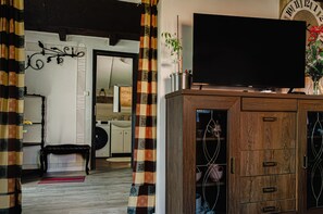 A living room with a television on a wooden cabinet, a bench, and a patterned curtain.