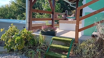 A covered outdoor area with a wooden structure, a paved walkway, and a garden with various plants.