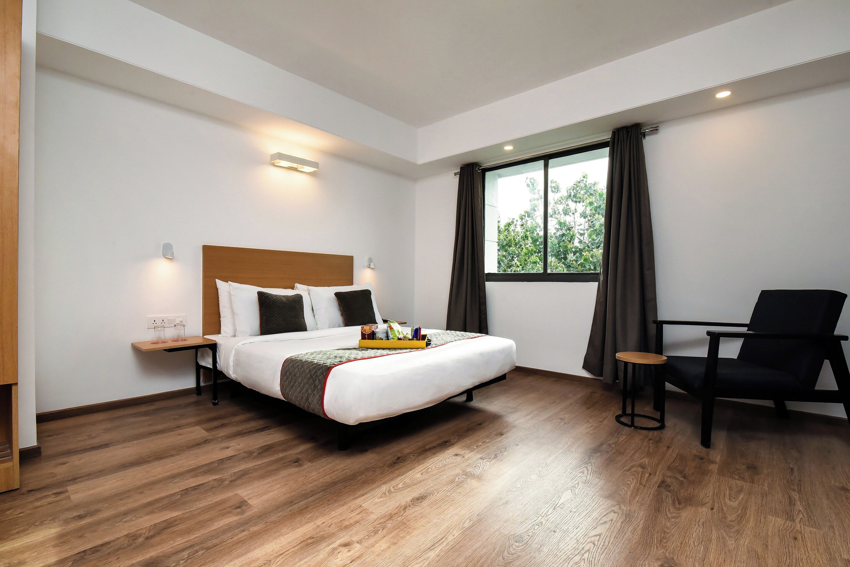 Une chambre d’hôtel avec un lit, une chaise, une petite table et une fenêtre avec des rideaux.