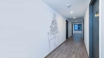 A hallway with a wooden floor, white walls, and a wall-mounted artwork depicting a tree with fruits and a figure.