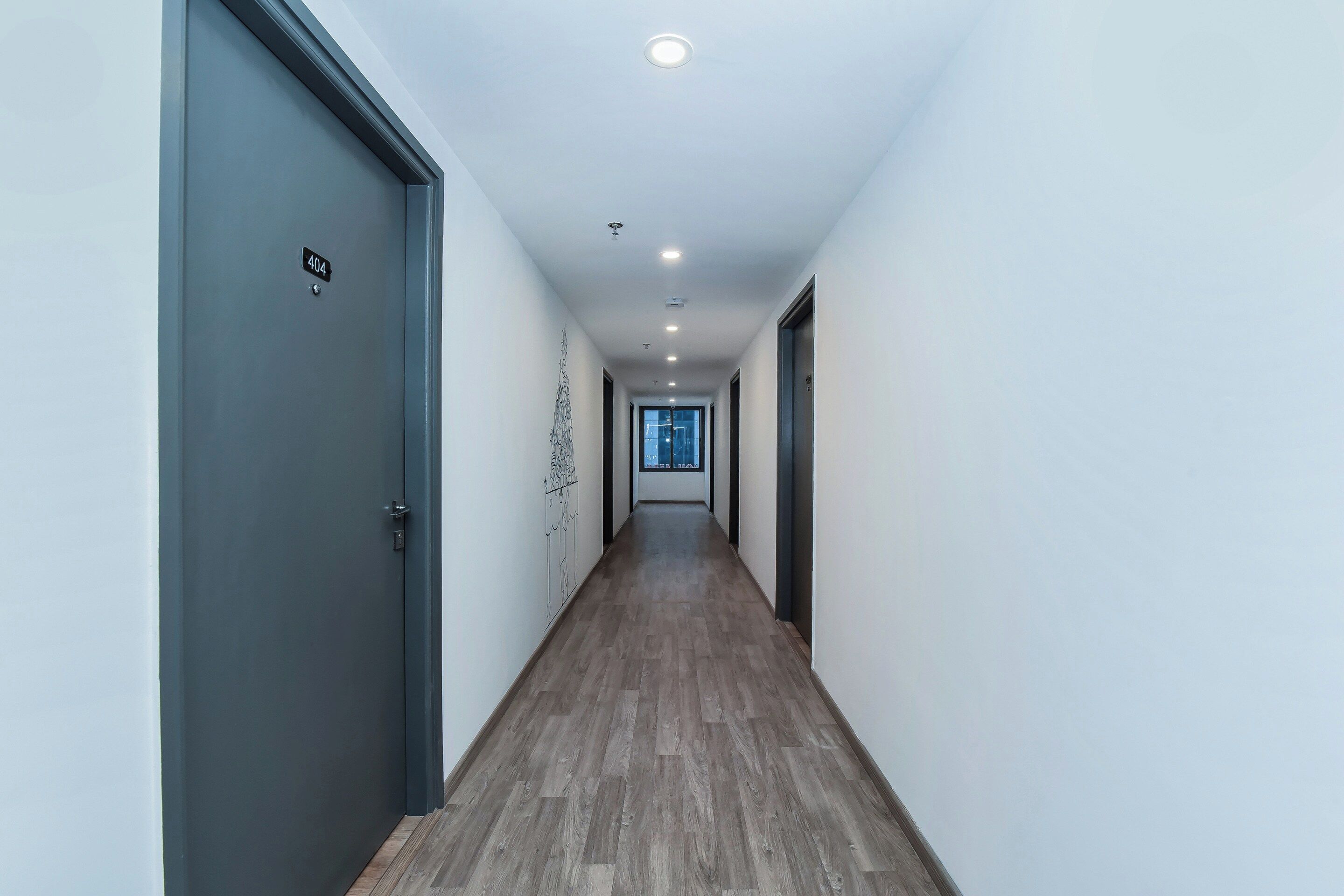 Un couloir doté d’un plancher en bois, de murs blancs et de portes de part et d’autre.
