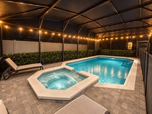 Une piscine couverte dotée de chaises longues et d’un jacuzzi, le tout entouré d’une clôture et illuminé de guirlandes lumineuses.