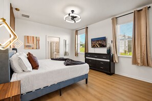Une chambre moderne comprenant un lit, une table de chevet, une commode et une grande fenêtre avec des rideaux.