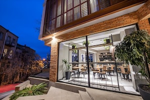 Ein modernes Gebäude mit großen Glasfenstern, einer Ziegel-Fassade und einem Sitzbereich mit Tischen und Stühlen.