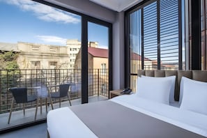Ein Hotelzimmer mit einem großen Bett, einem Balkon mit Sitzgelegenheiten und Blick auf die Stadtlandschaft.