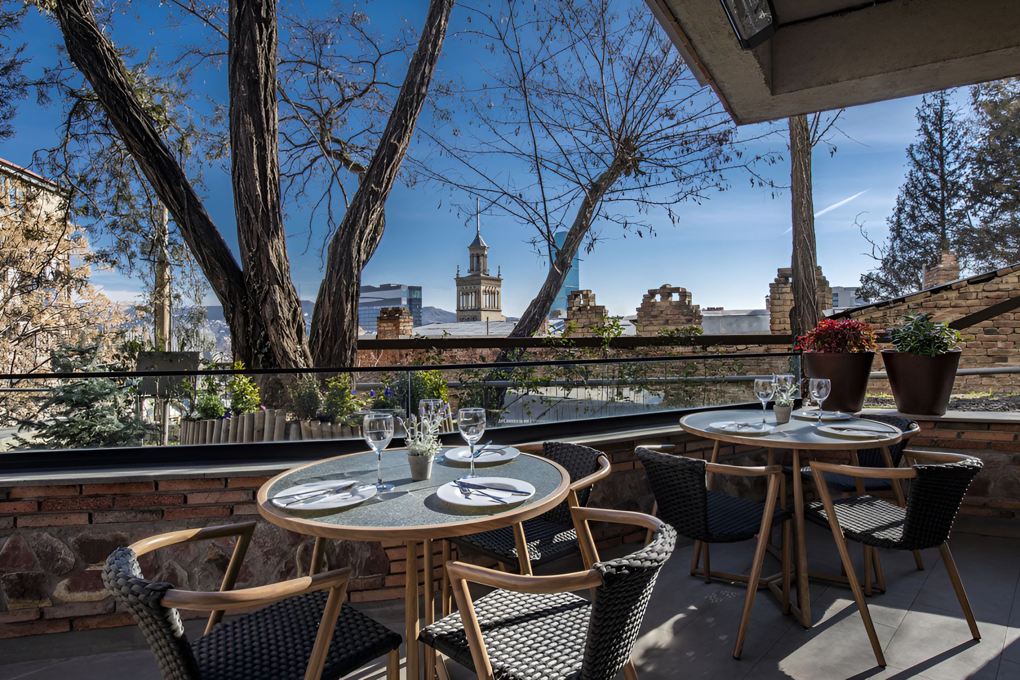 Una terrazza esterna con tavoli e sedie rotonde, vista su un edificio storico e cielo sereno.