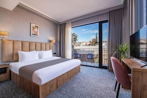 Ein Hotelzimmer mit einem großen Bett, einem Schreibtisch und Blick auf die Stadt durch das Fenster.