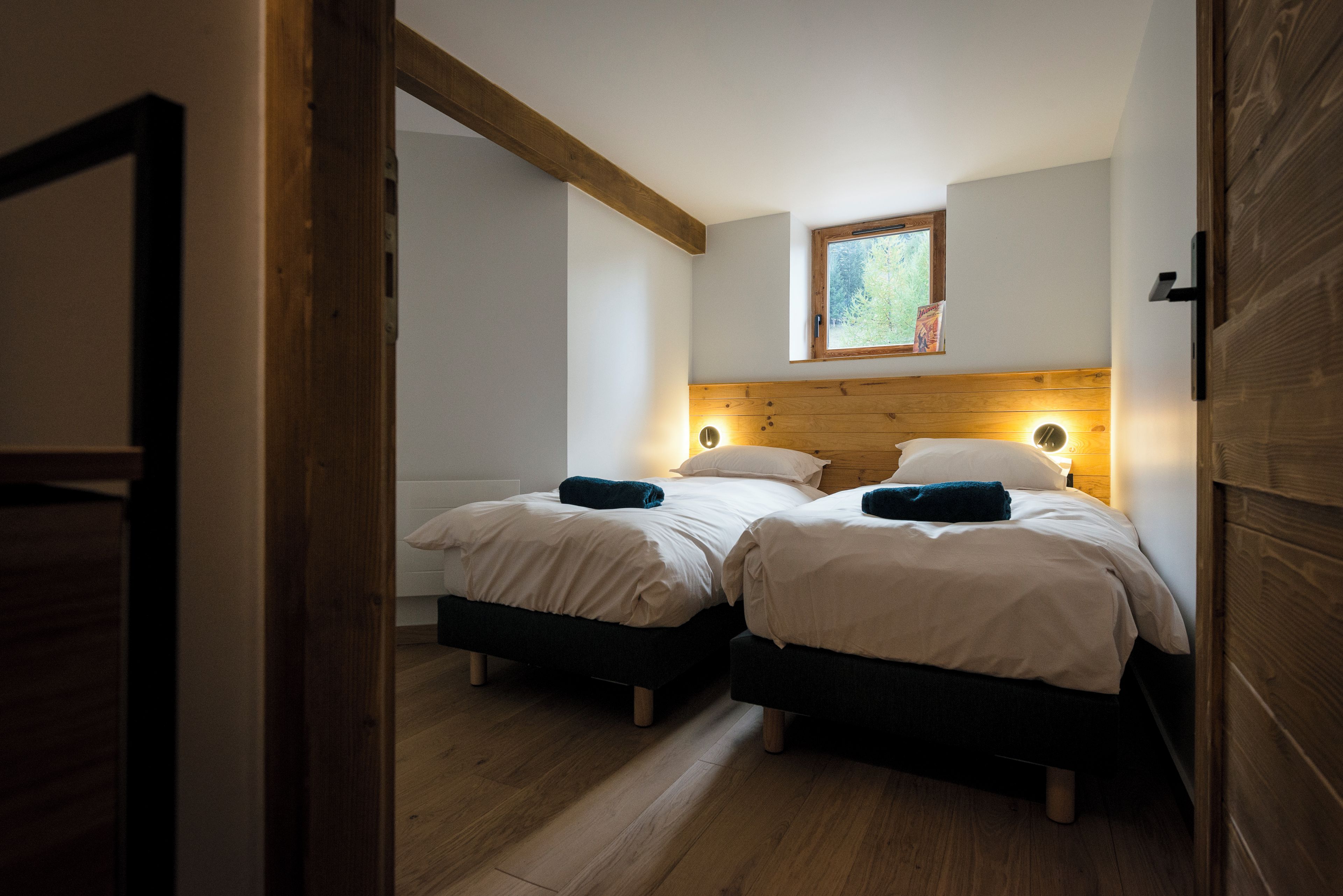 A bedroom with two beds, wooden headboards, a small window, and a wooden floor.