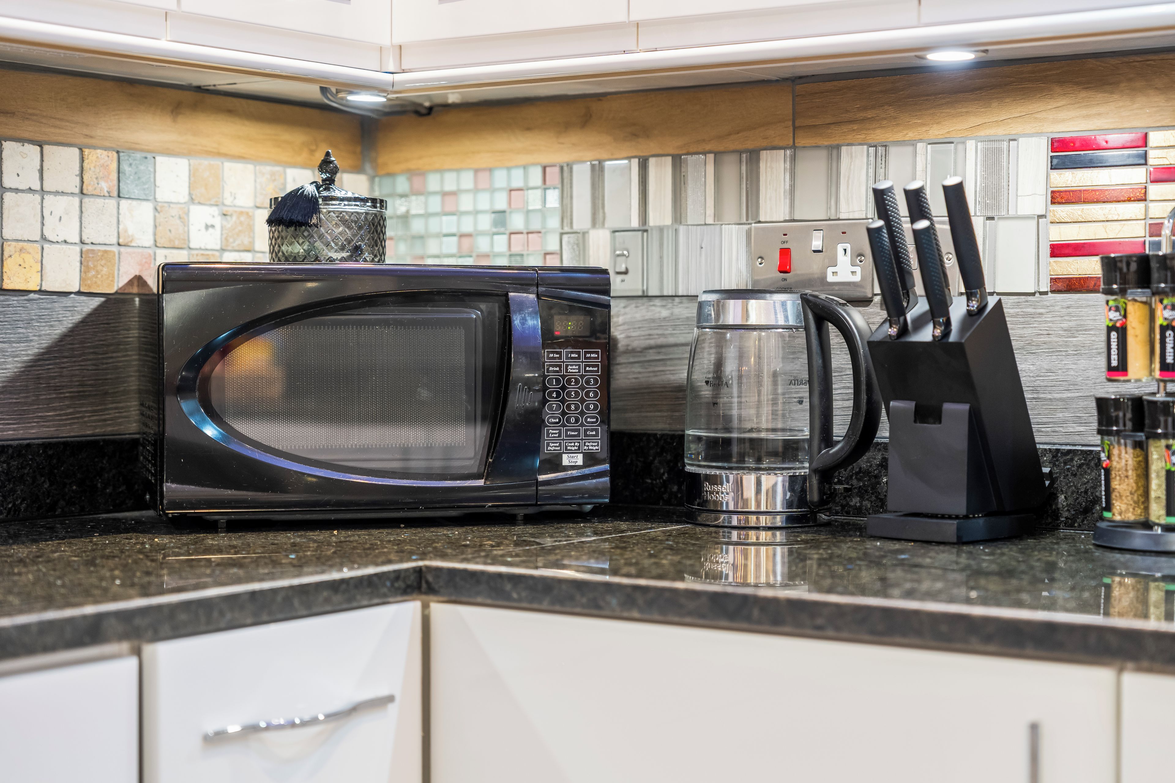 A kitchen with a microwave, a kettle, and a knife block.