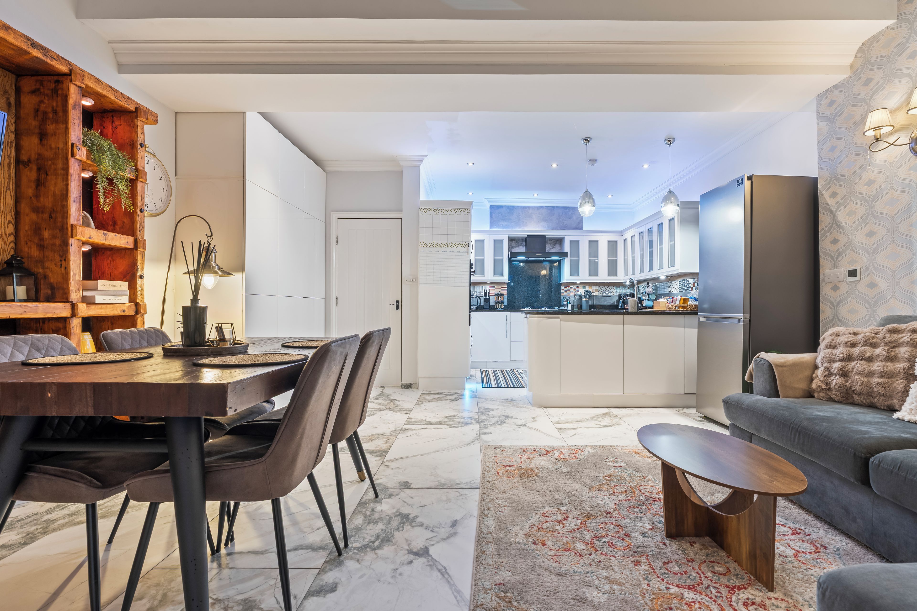 A modern living room with a dining area, a kitchen with a central island, and a grey sofa.