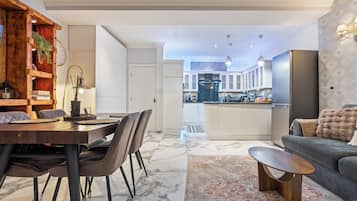 A modern living room with a dining area, a kitchen with a central island, and a grey sofa.