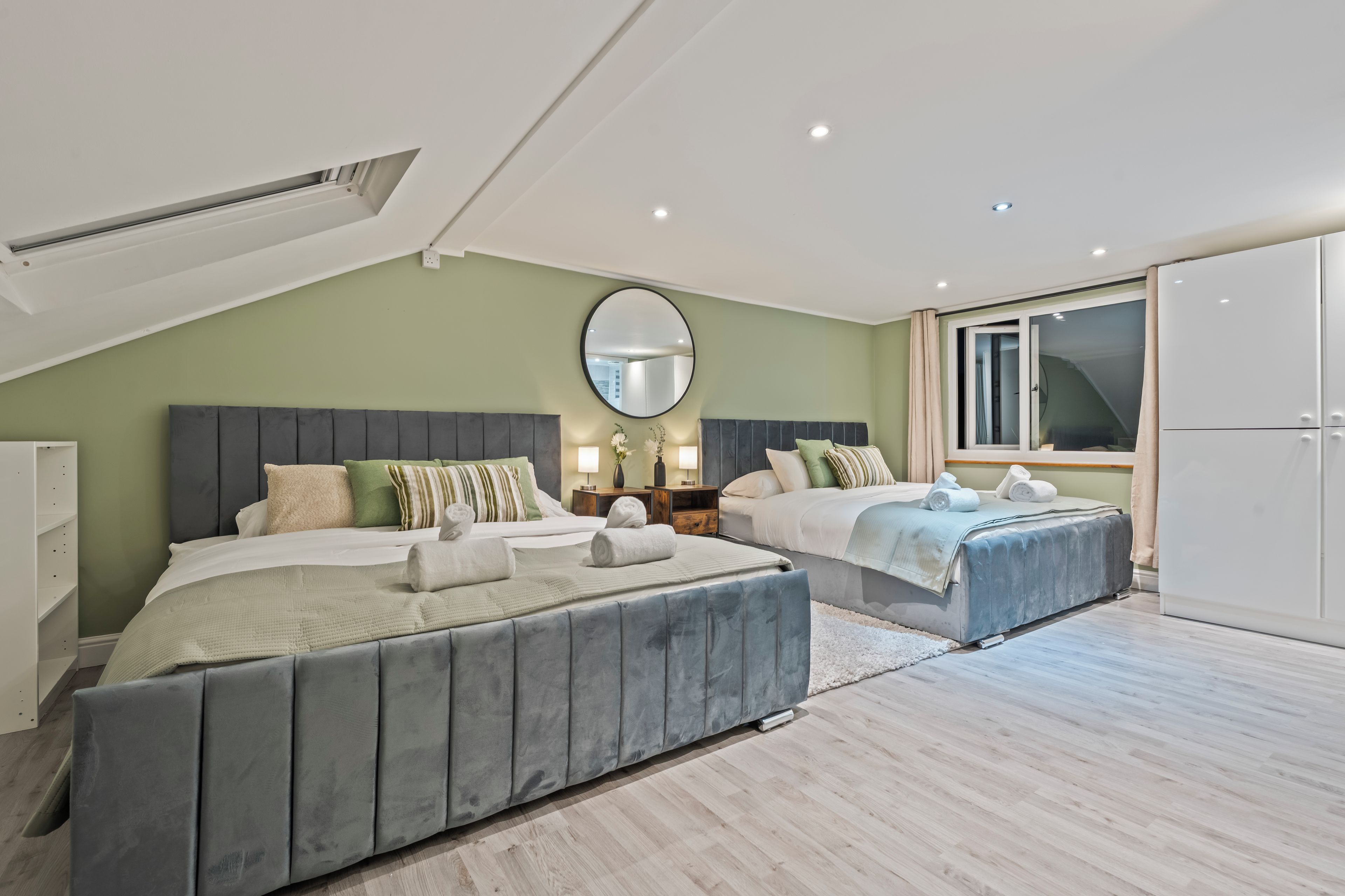 A modern bedroom with two beds, a large mirror, and a sliding glass door.