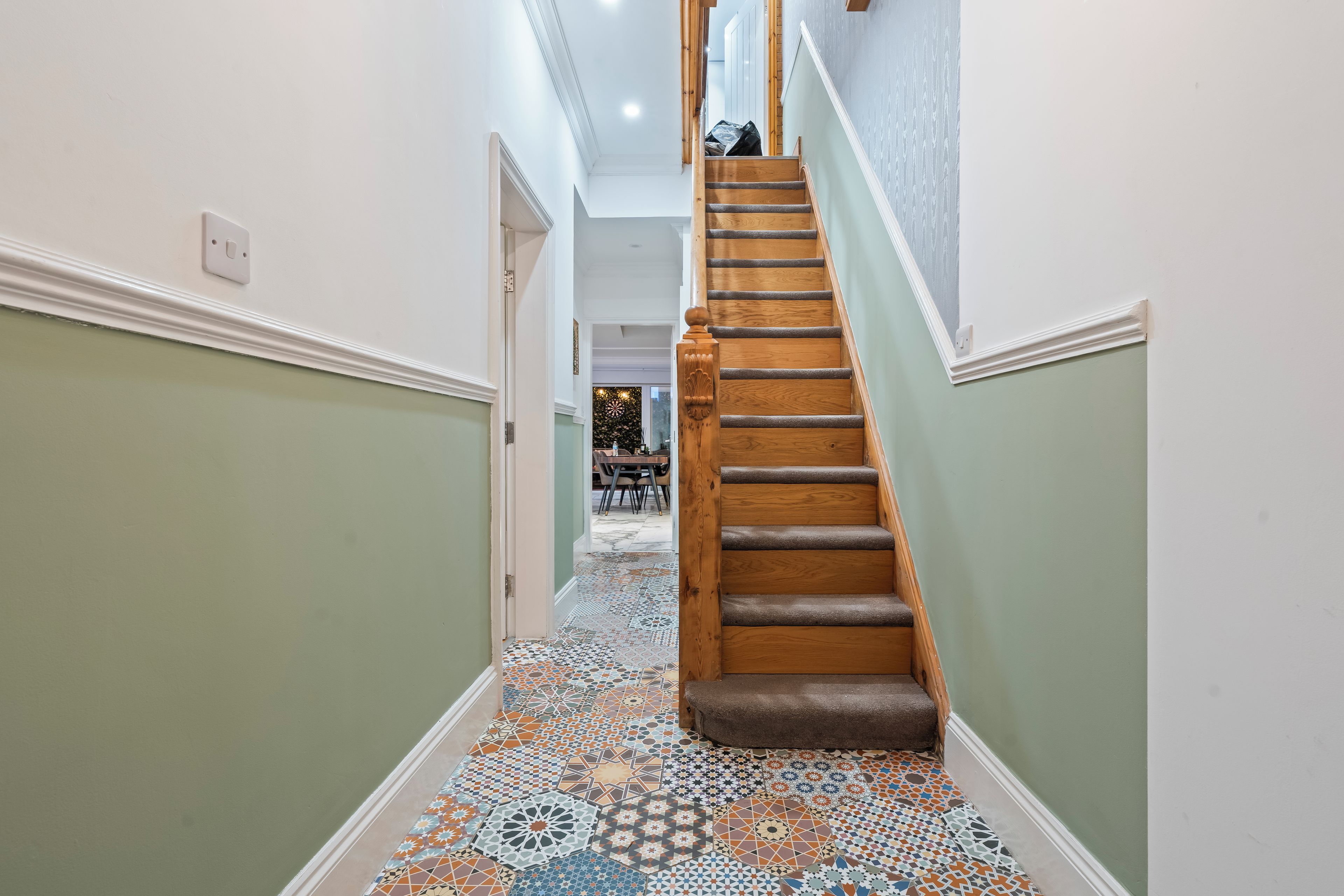A hallway with a wooden staircase leading to a dining area.