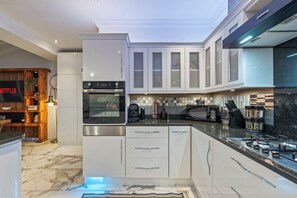 A modern kitchen with white cabinetry, a built-in oven, a coffee machine, and a microwave. - Willowtree (Liverpool)