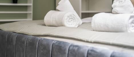 A neatly made bed with rolled white towels and a quilted blanket.
