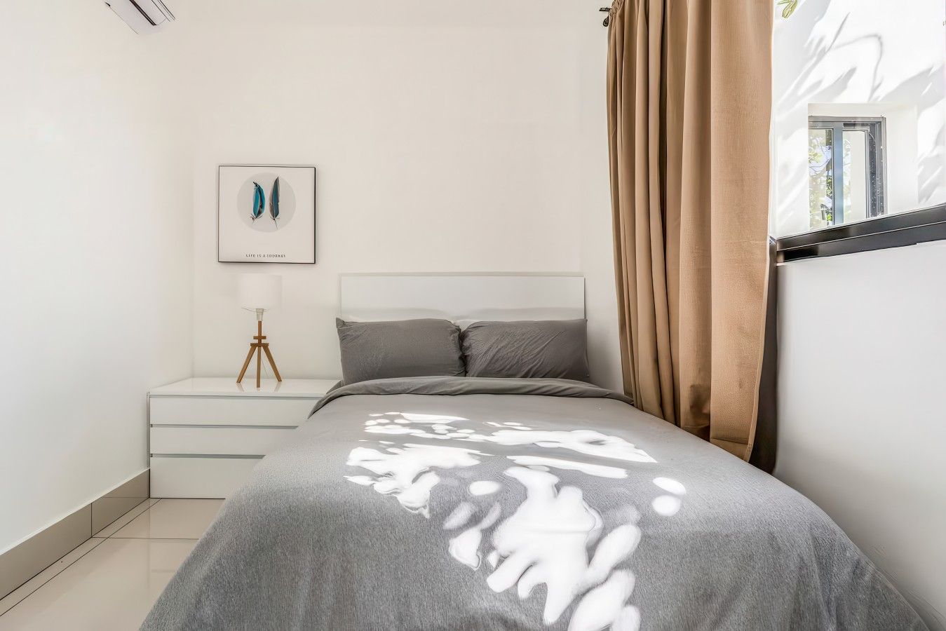 Une chambre à coucher avec un lit, une table de chevet, un tableau encadré et une fenêtre avec des rideaux.