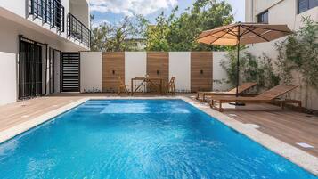 Une piscine avec une terrasse en bois, des chaises longues et une table.