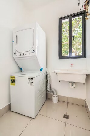 A compact laundry room with a front-loading washing machine, a sink, and a window. - Nazar Suites - Entire 8-Bedroom Estate with Private Pool (Santiago de los Caballeros)