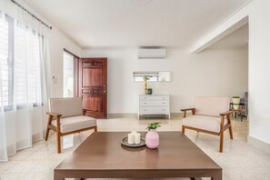 A room with two chairs, a coffee table, a dresser, and a door. - Nazar Suites - Unit 1A   (Santiago de los Caballeros)
