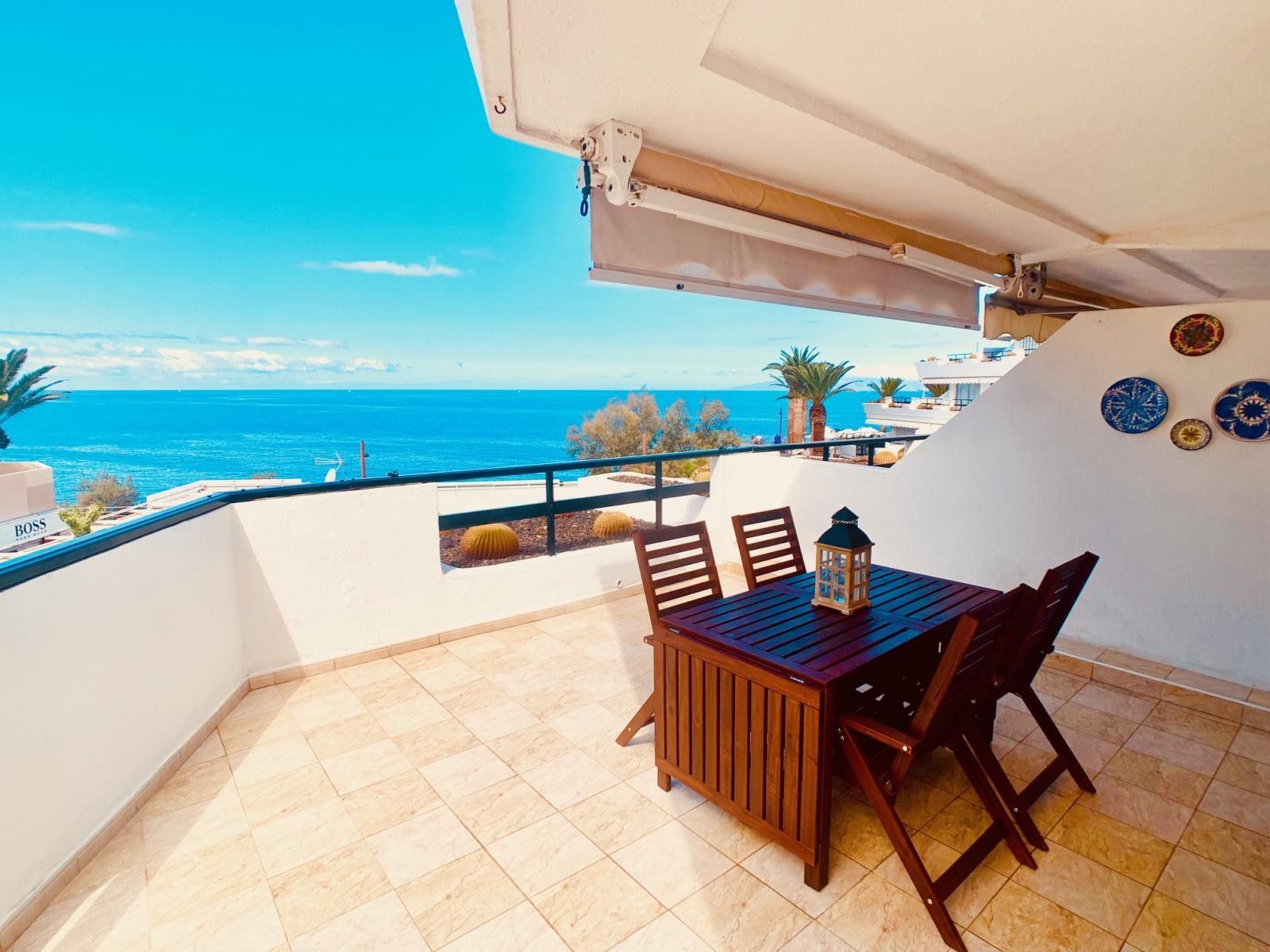 Een balkon met een tafel en stoelen, met uitzicht op de kust.