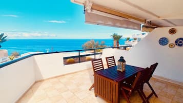Een balkon met een tafel en stoelen, met uitzicht op de kust.