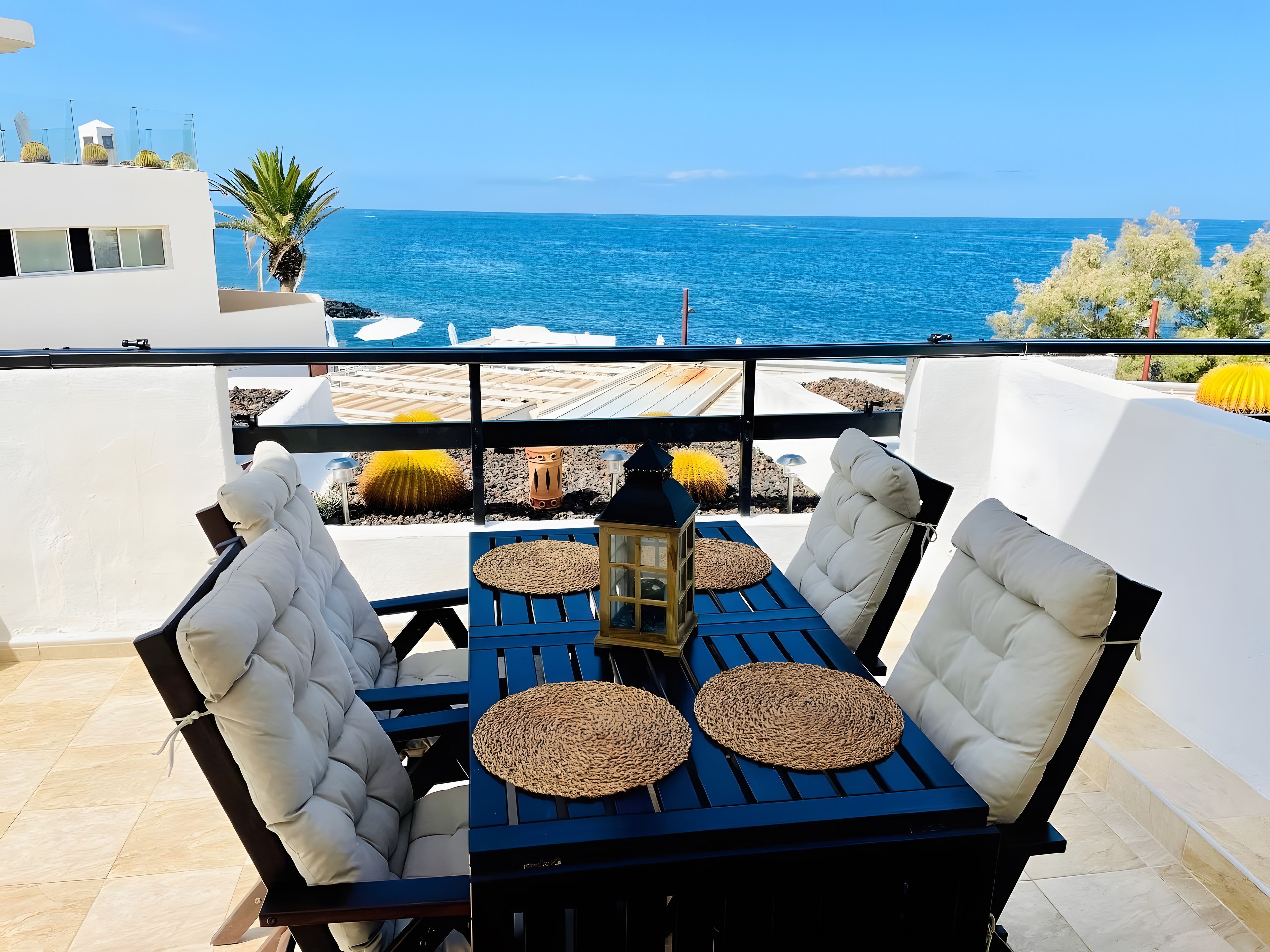 Une terrasse avec une table et des chaises, une lanterne et une vue sur la mer.
