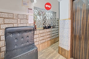 Un área de recepción con mostrador de entrada, escritorio de recepción y una zona de estar con sillón acolchado.