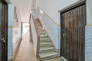 Un pasillo estrecho con un muro de azulejos, una puerta de madera y una escalera con barandilla de cerámica.