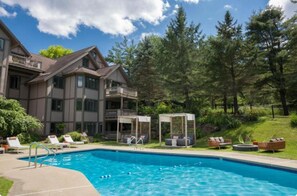 Un hotel con piscina, mobiliario exterior y zonas arboladas.