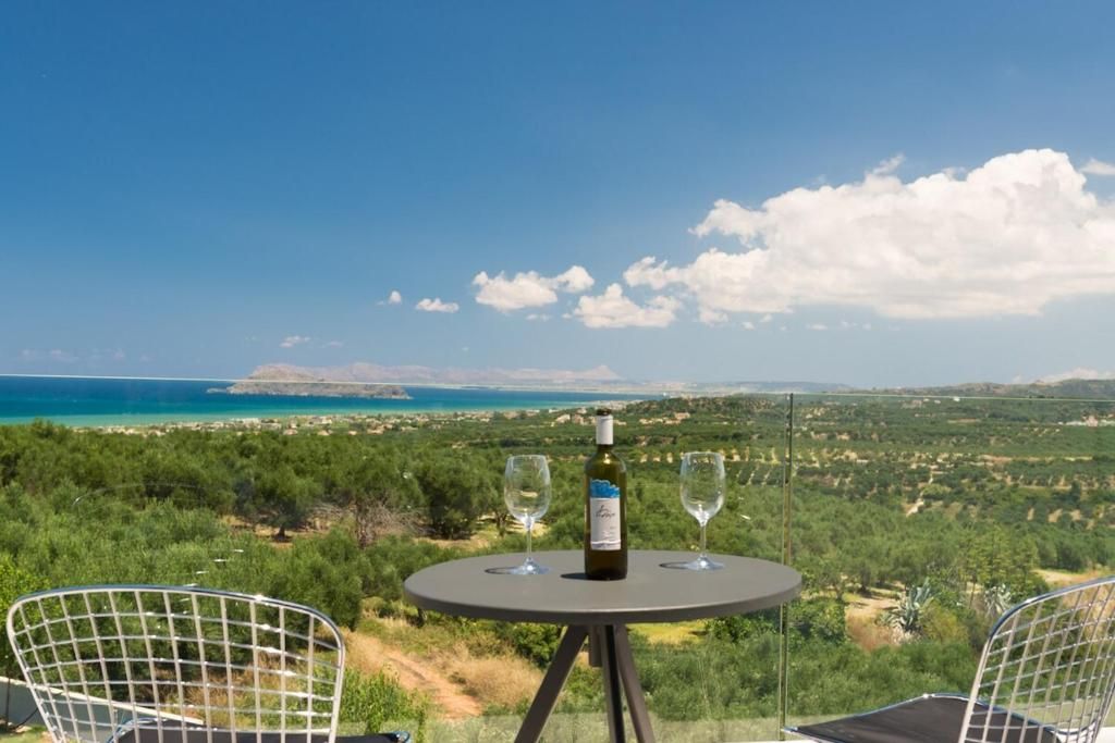 Ein Tisch mit einer Weinflasche und zwei Gläsern, mit Blick auf eine Küstenlandschaft mit Bäumen und Meer.