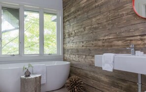 Un baño con pared de madera, una bañera, un lavamanos y un ventanal.