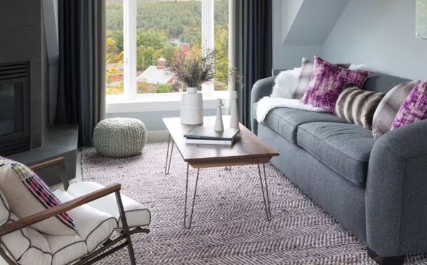 Una sala de estar moderna con un sofá gris, una mesa de centro de madera y un reposapiés blanco.