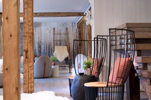 Una habitación acogedora con techo de madera, un sofá y una silla de diseño original con estructura metálica.