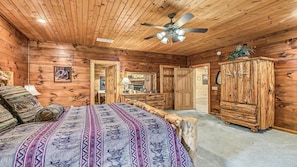 A log cabin bedroom with a bed, dresser, and ceiling fan. - Timberstone: Luxury 4BR Cabin, Pool table, Arcade, Hot Tub, & Resort Pool (Sevierville)